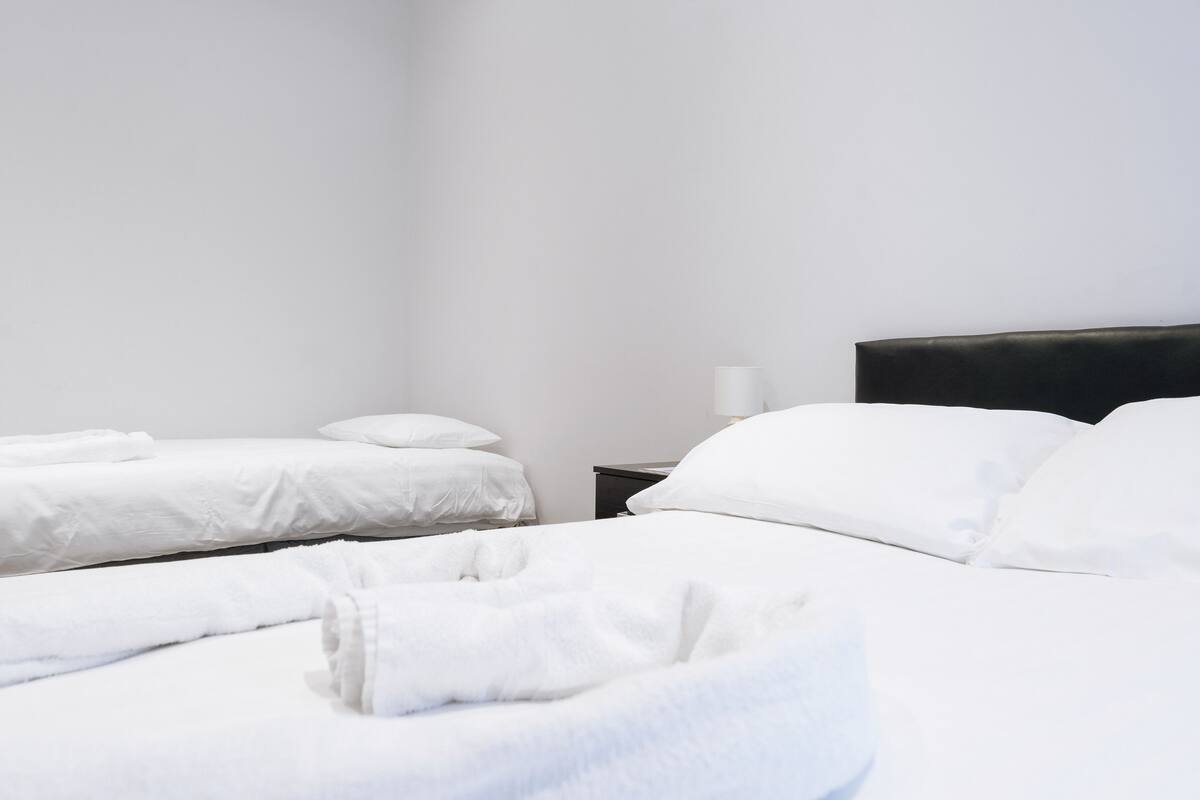 A hotel room with two beds, white linens, a black headboard, and a nightstand with a lamp.