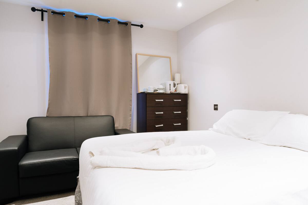 A bedroom with a bed, a black leather sofa, a dresser, and a mirror.