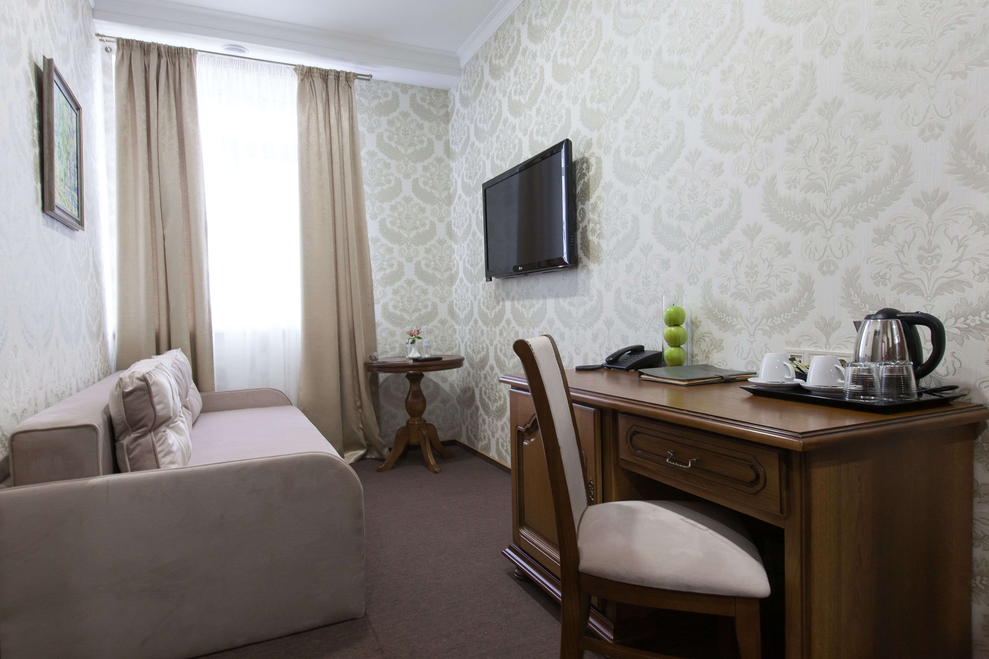 Una habitación de hotel con sofá, un escritorio de madera con teléfono, cafetera y televisión en la pared.