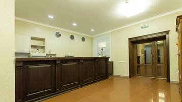 A reception area with a dark wooden reception desk, a clock, and a sign indicating the direction to the bathroom.