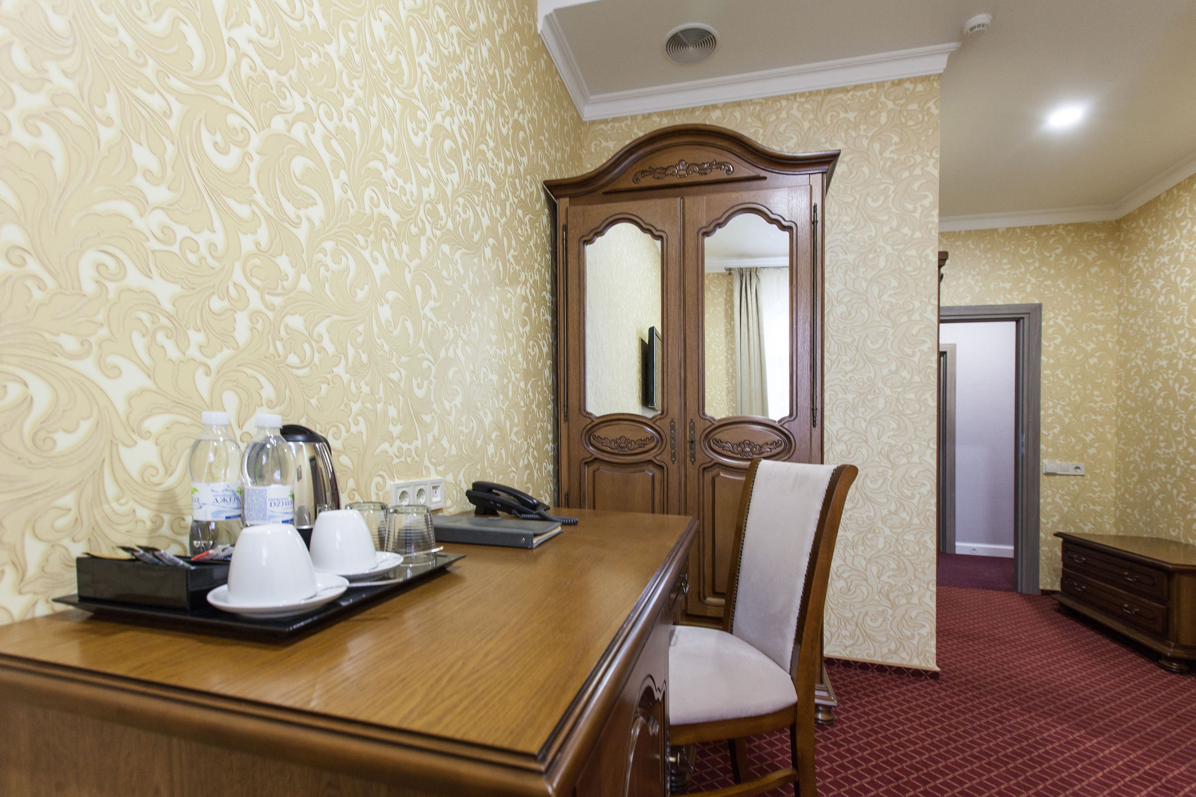 A hotel room with a wooden desk, two chairs, a telephone, and a mirror.