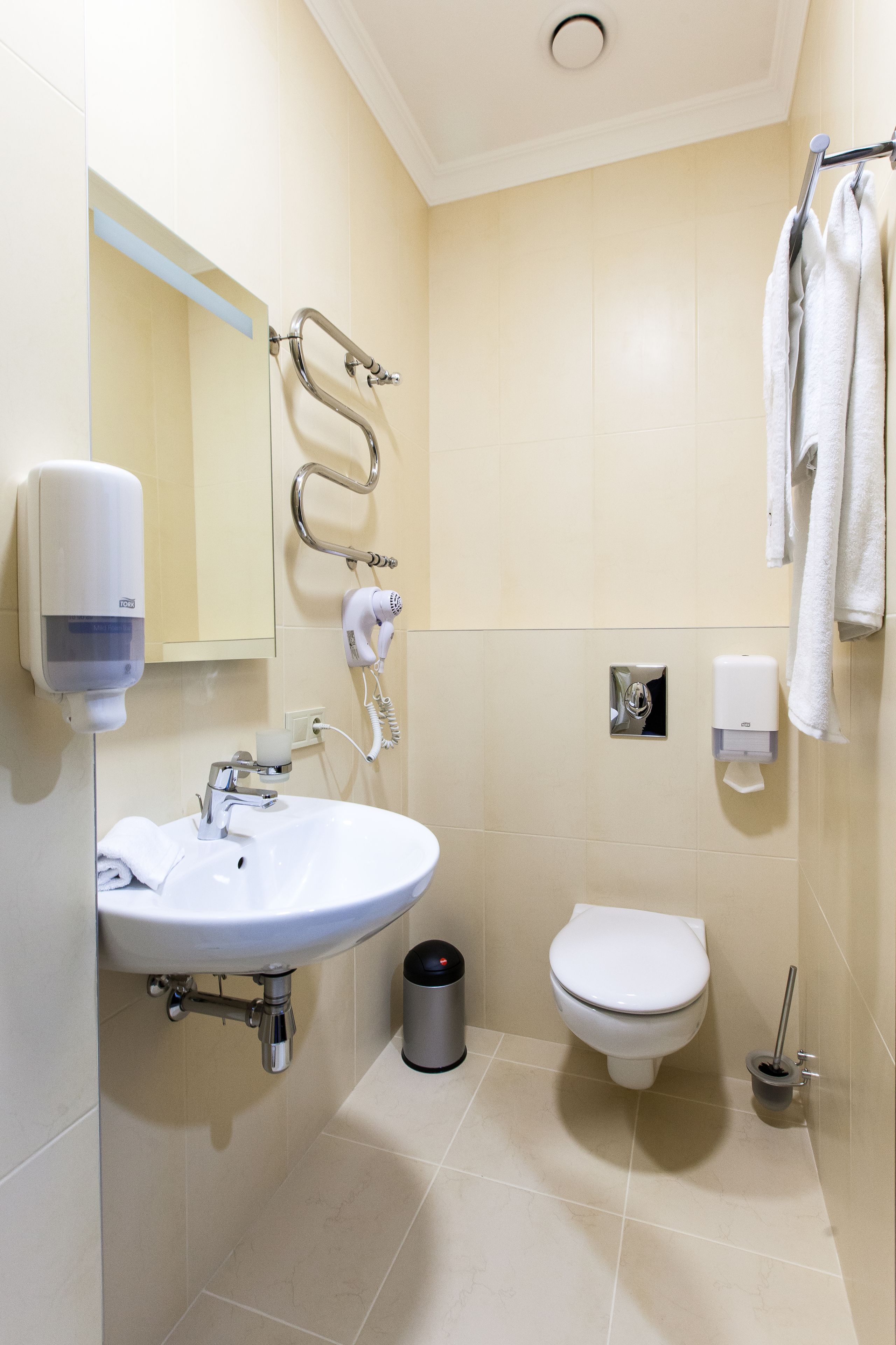 A modern bathroom with a sink, toilet, hand dryer, and towel dispenser.