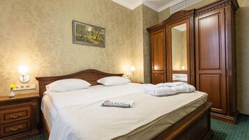 A neatly made bed with white linens, a wooden nightstand with a lamp, a dresser, and a large mirror.