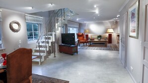 A spacious living room with a staircase, a television, and a dining area with a red chair. - Ferienwohnung Rosen/horstweg 5 (Sylt)