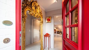 A hallway with a red door, a gold ornate mirror, and a small table with a red object on it. - Ferienwohnung Rosen/horstweg 5 (Sylt)