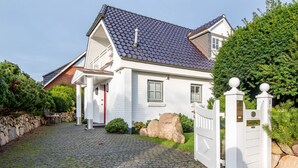 A white house with a tiled roof, a paved driveway, and a white gate. - Ferienwohnung Rosen/horstweg 5 (Sylt)