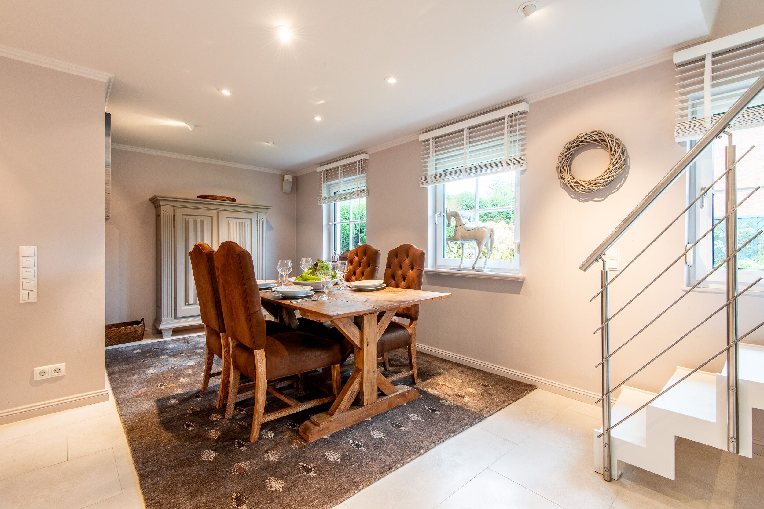 Un espace repas avec une table et des chaises en bois, un tapis et un escalier.