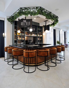A bar area with a black counter, multiple bar stools, and a sign reading "HOTEL DELLO TAPESTRY COLLECTION by Hilton".