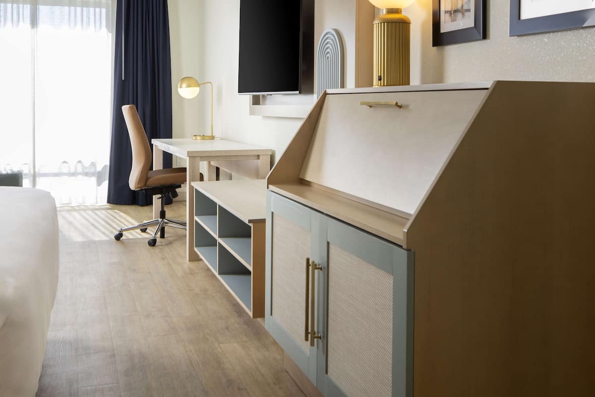 Ein Hotelzimmer mit Bett, Schreibtisch, Stuhl und einem an der Wand befestigten Fernseher.