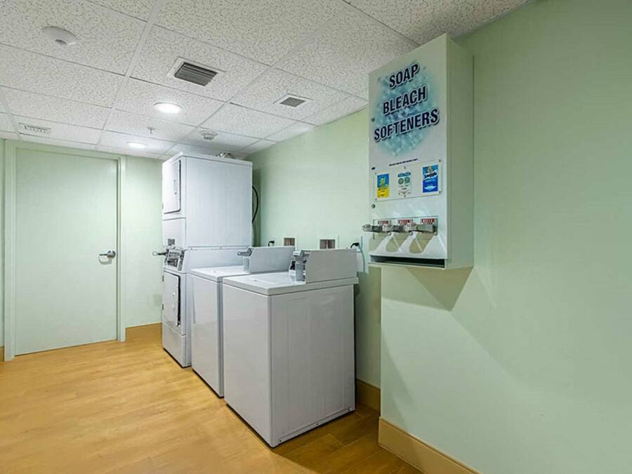 Zona de bugaderia amb dues rentadores i dues assecadores, un dosificador de sabó, lleixiu i suavitzant, i una porta a un altre espai.