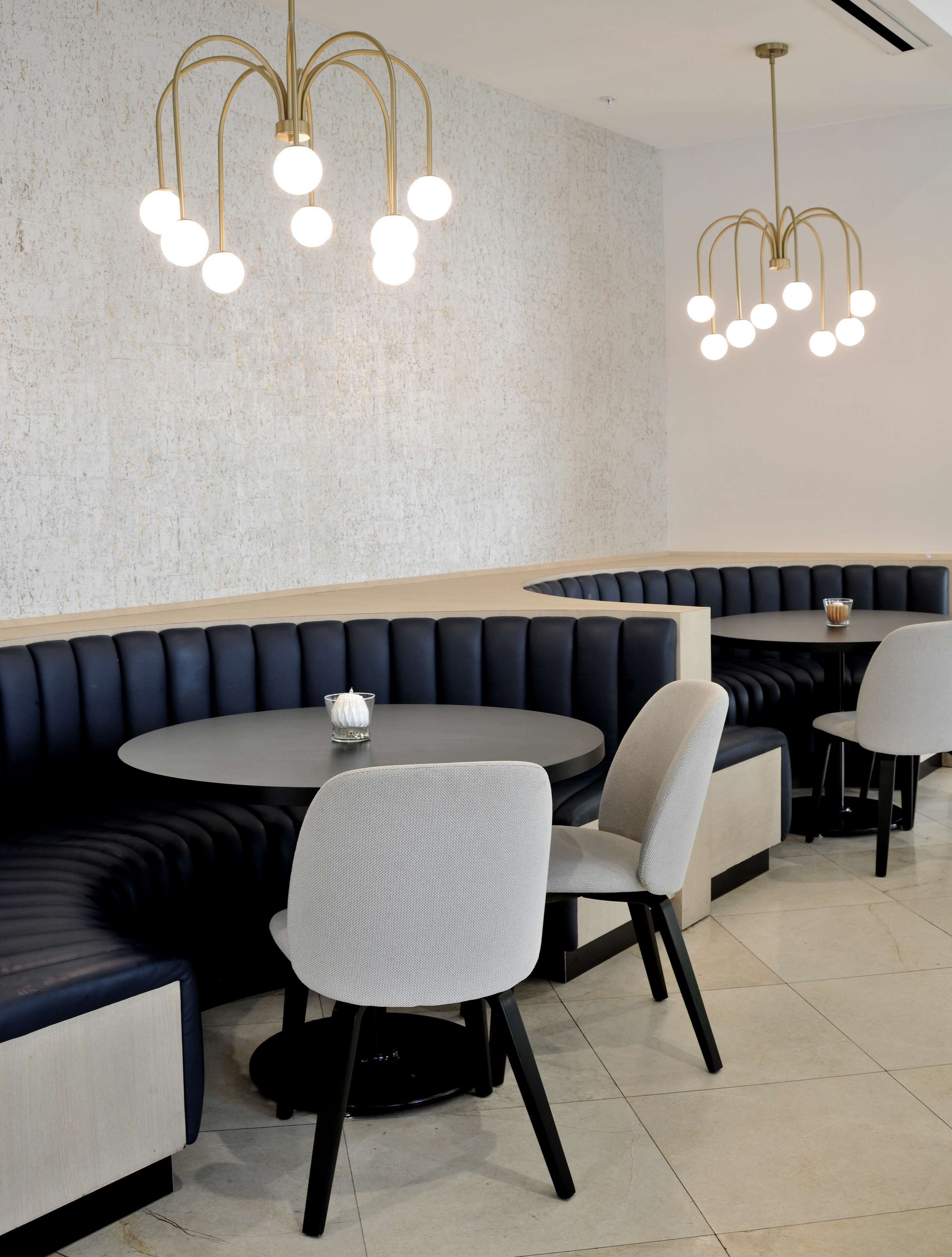 A restaurant with round tables, dark cushioned booths, and modern chandeliers.