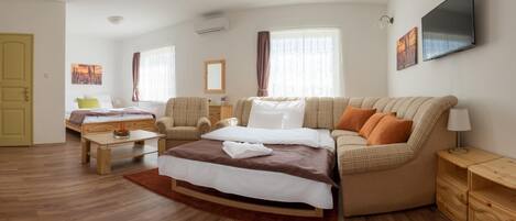 A modern hotel room with a large bed, a sofa, a desk, and a TV.