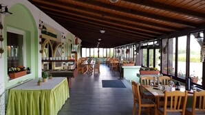 Un restaurante con patio cubierto, mesas y sillas de madera, y ventanas amplias con vistas al exterior.