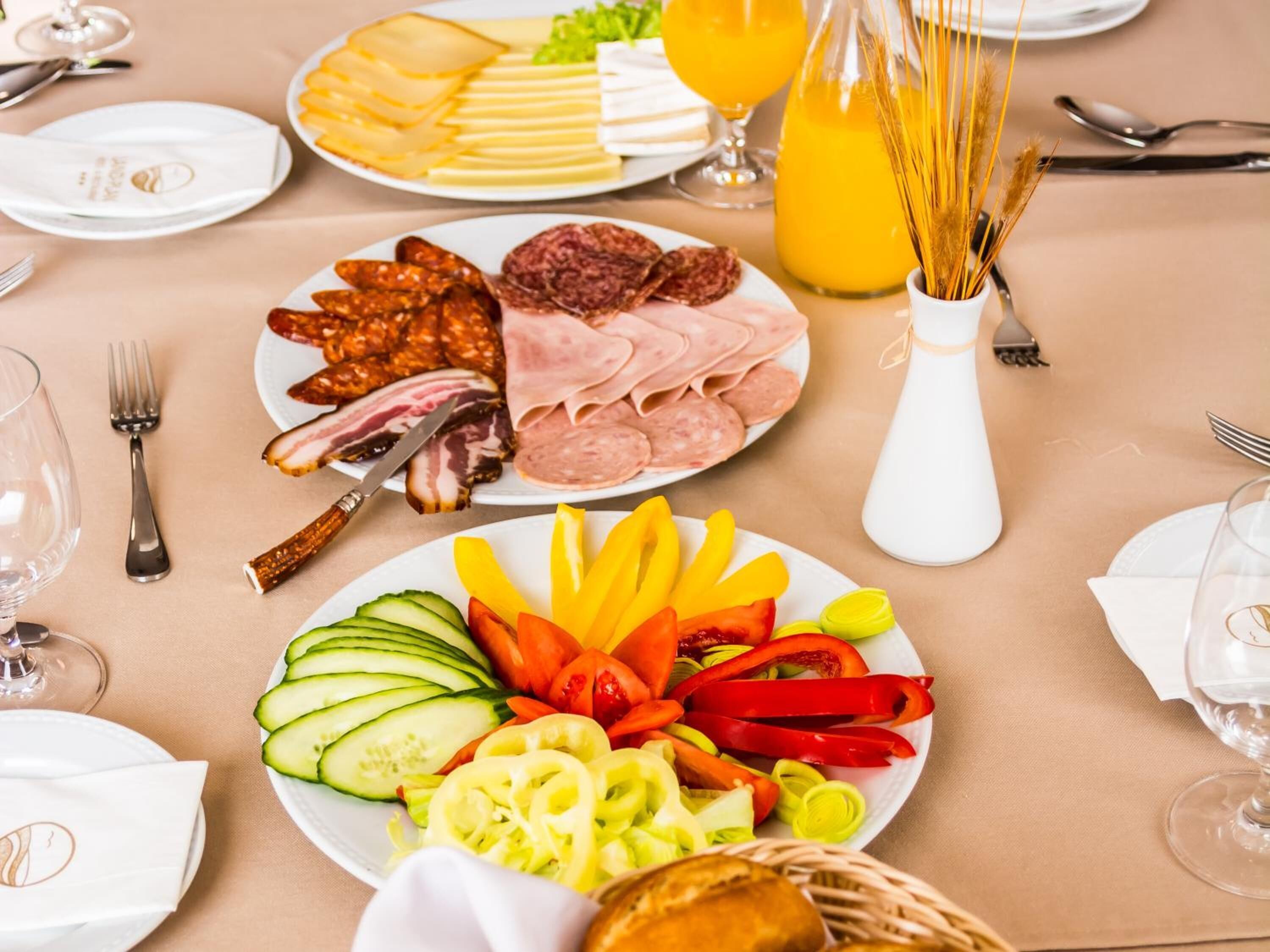 A breakfast buffet with various meats, cheeses, and fresh vegetables.
