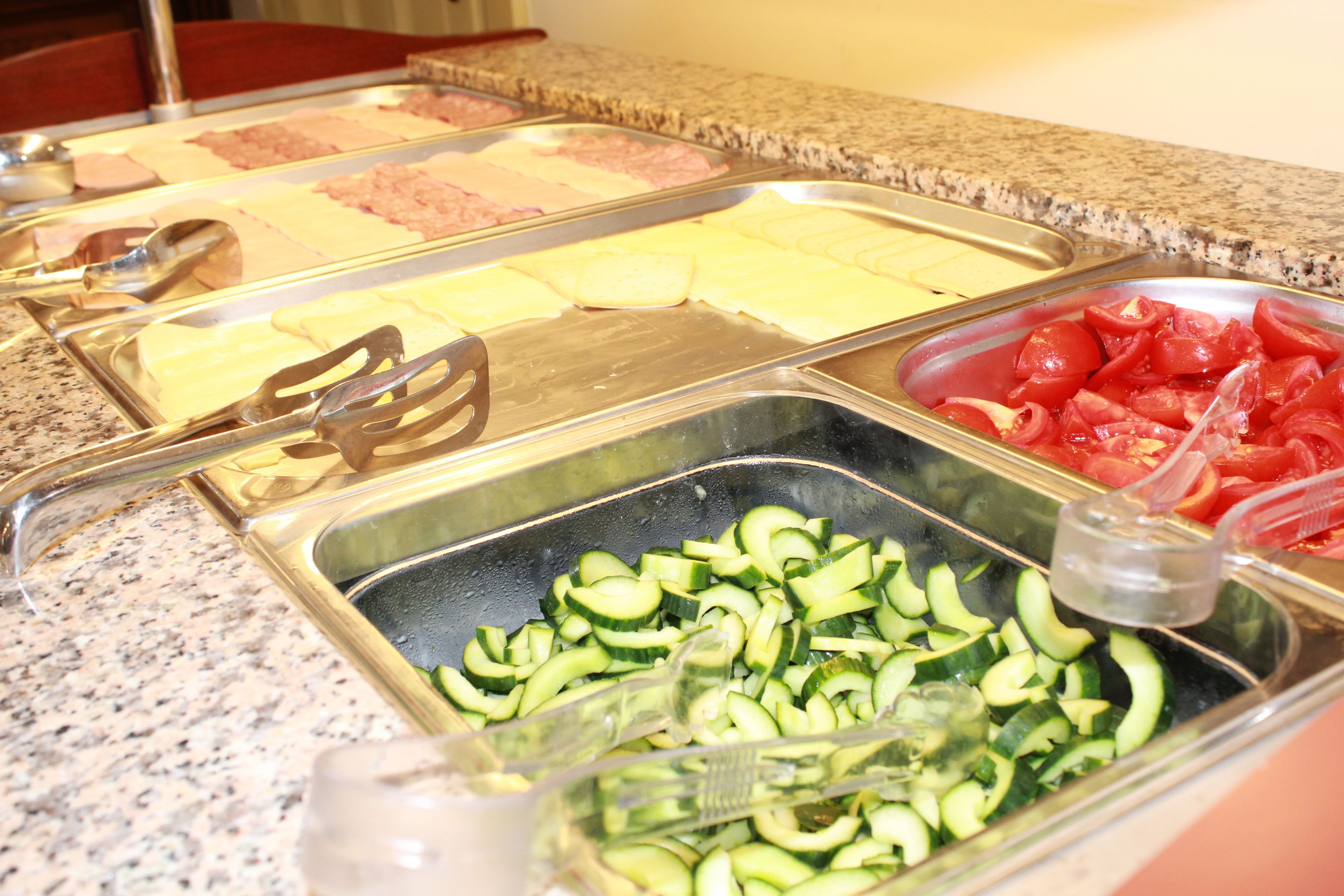 Un bufé con diversas opciones de comida, incluyendo pepinos en rodajas, tomates y diferentes tipos de carne.