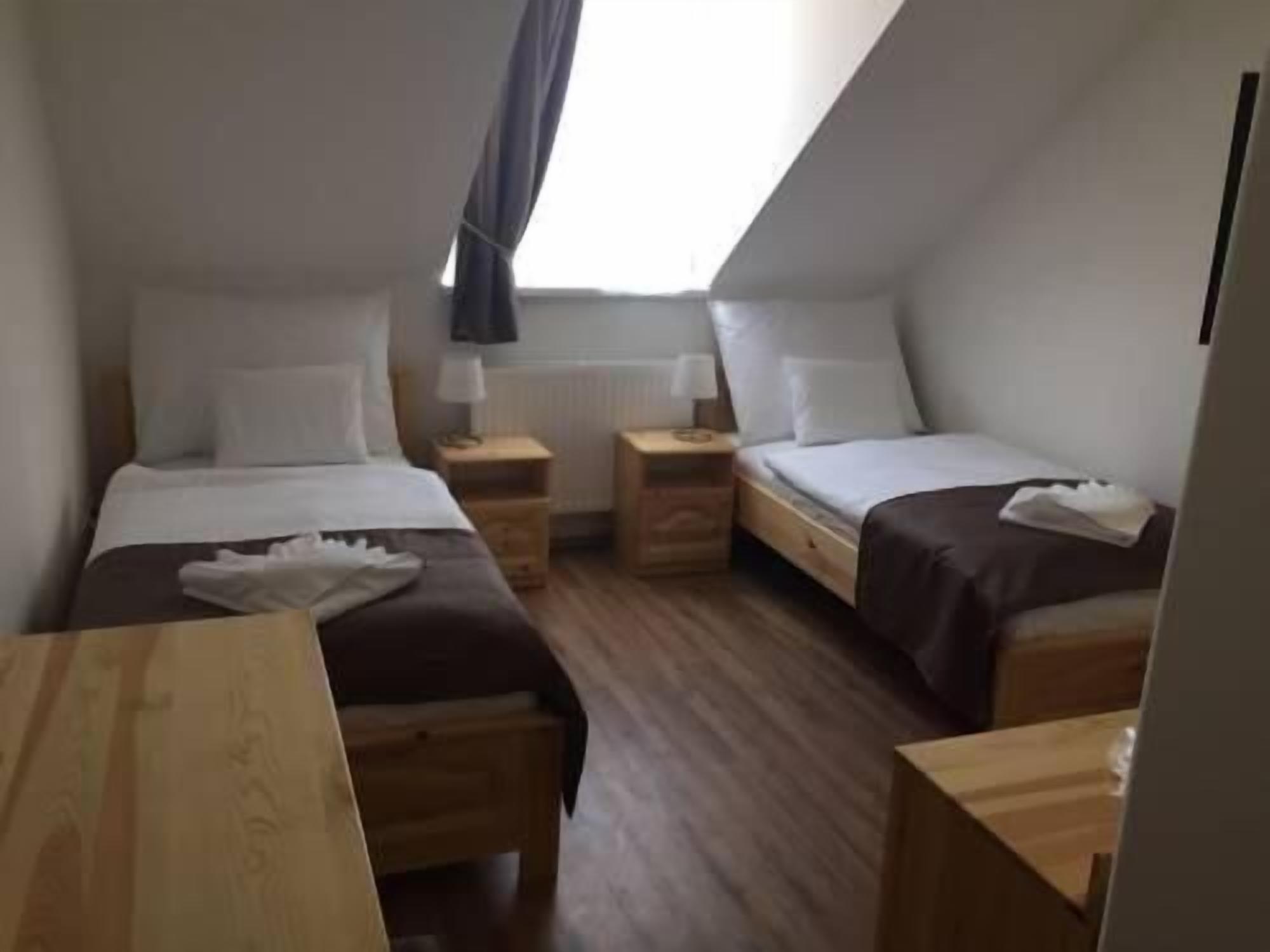 A small, cozy room with two single beds, wooden nightstands, and a small table.