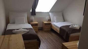 A small, cozy room with two single beds, wooden nightstands, and a small table.