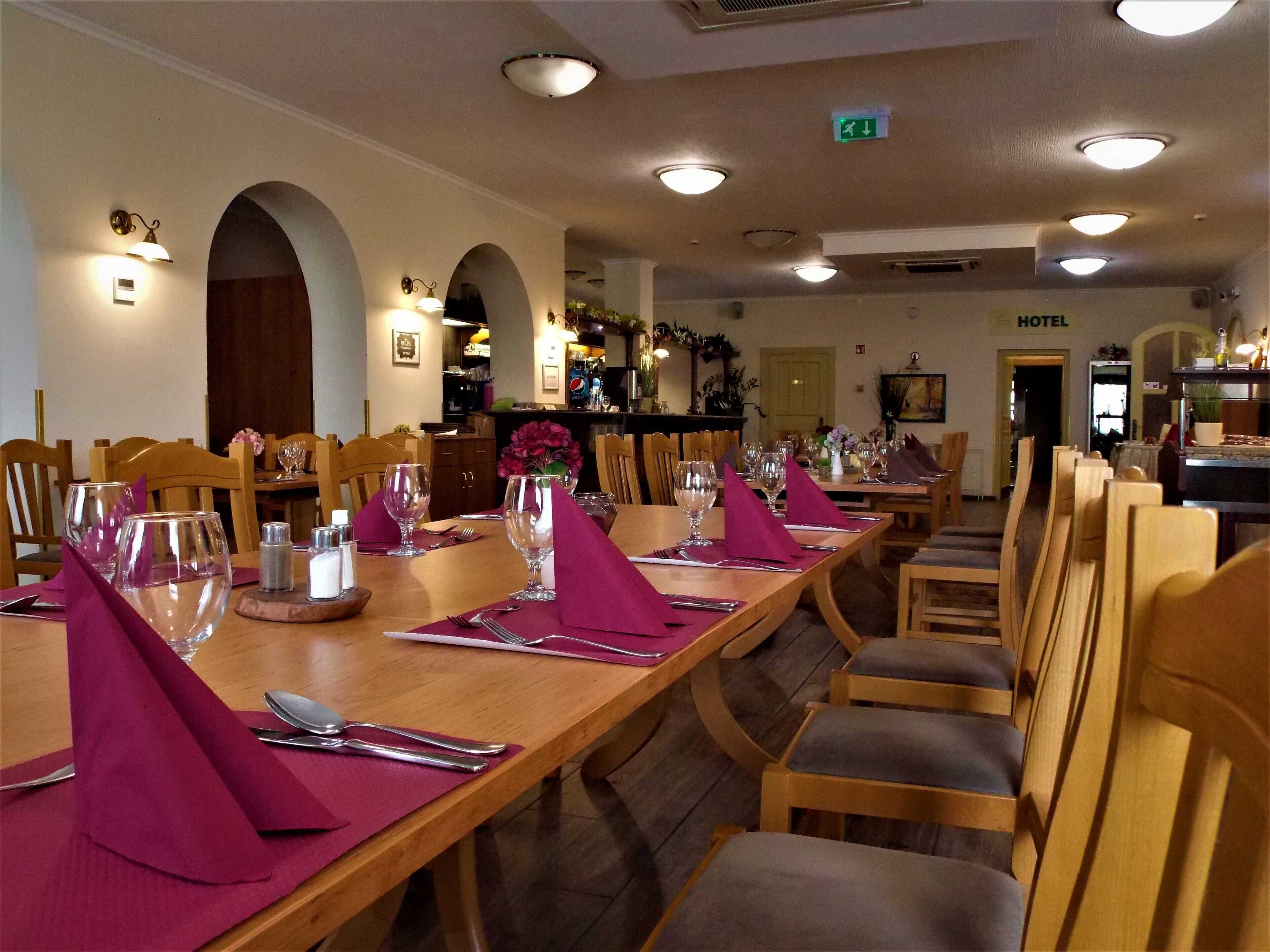 Un comedor con largas mesas de madera dispuestas para varios invitados, con copas de vino, cubiertos y servilletas.