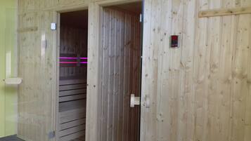 A wooden interior with a sliding door leading to a room with a control panel and pink lighting.