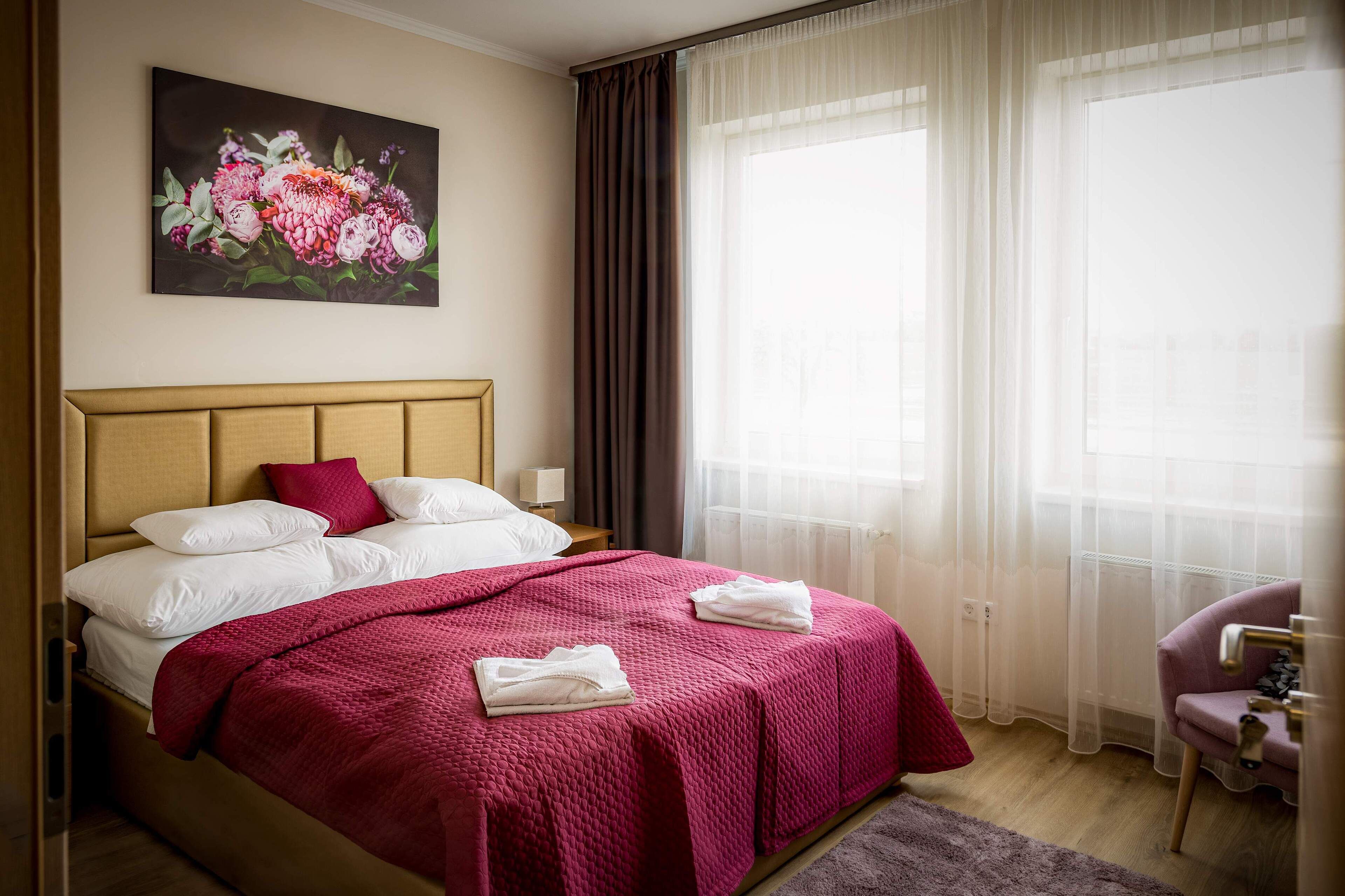 Una habitación de hotel con cama, un cuadro, una silla y una ventana con cortinas.