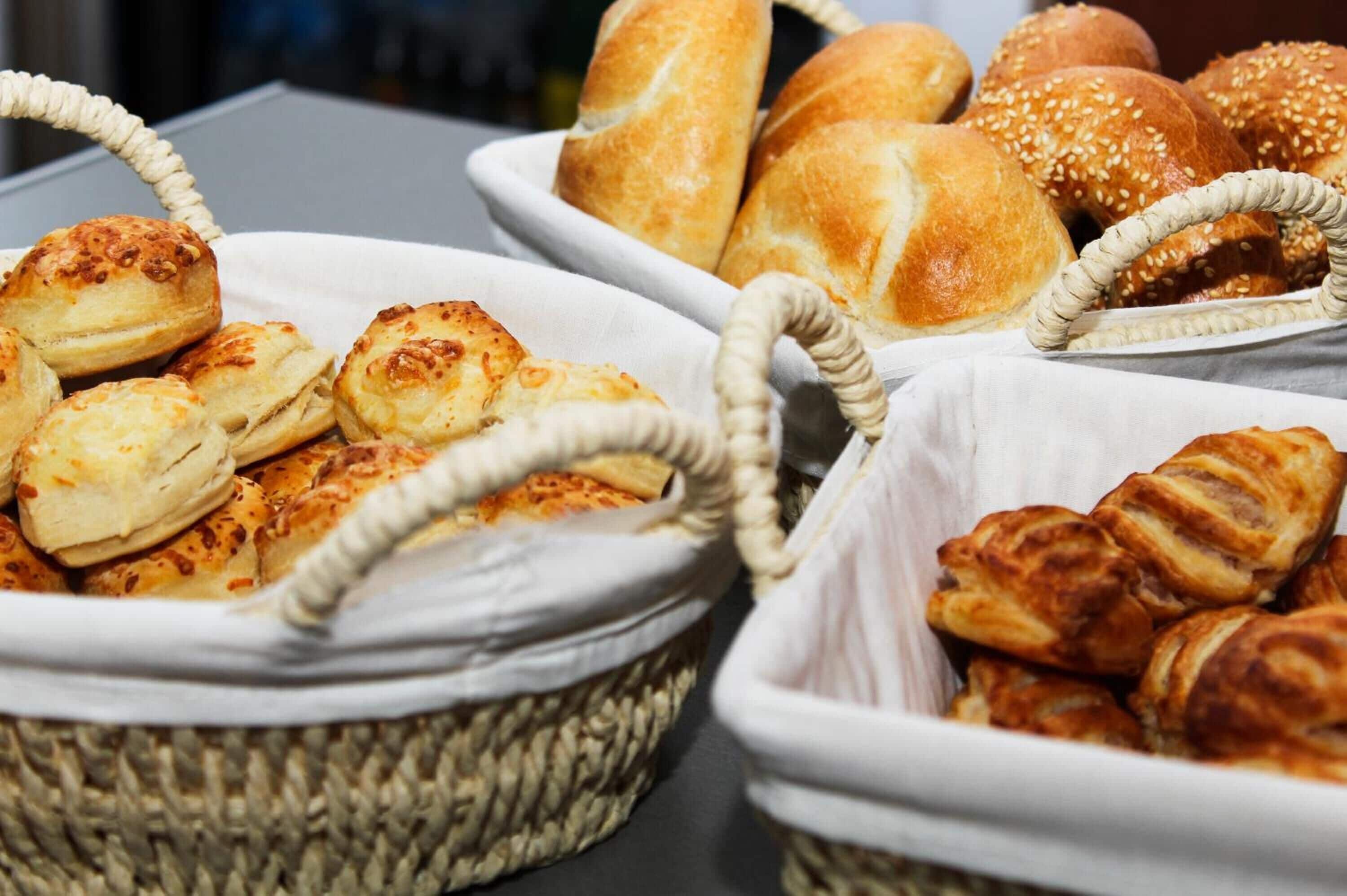 Diversos produtos de panificação em cestas, como pães, brioches e doces.