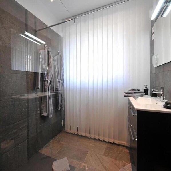 Une salle de bain moderne dotée d’un grand miroir, d’une zone douche et d’un meuble-lavabo avec un évier.