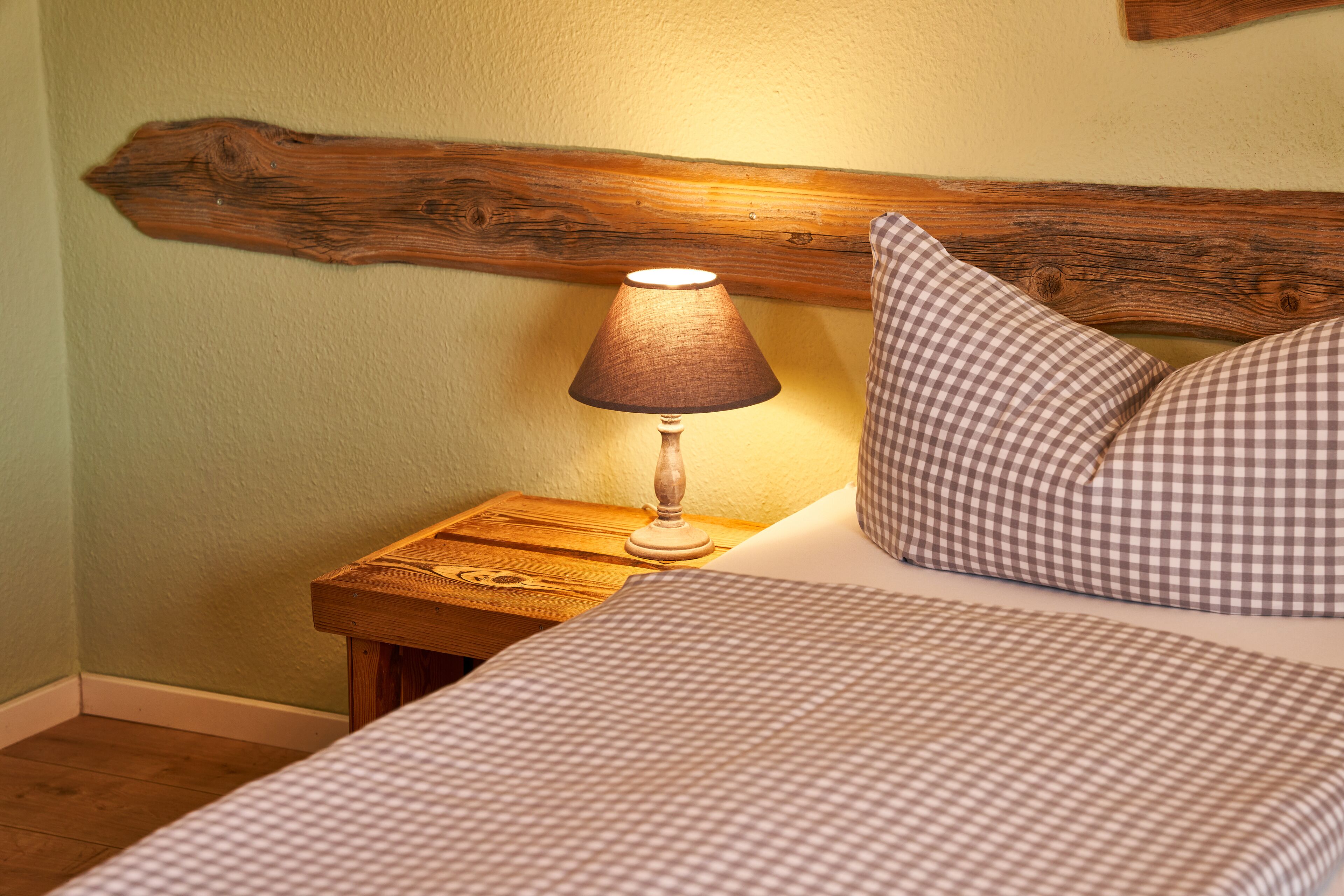 A bed with a checkered bedspread and pillows, a wooden nightstand with a lamp, and a wooden headboard.