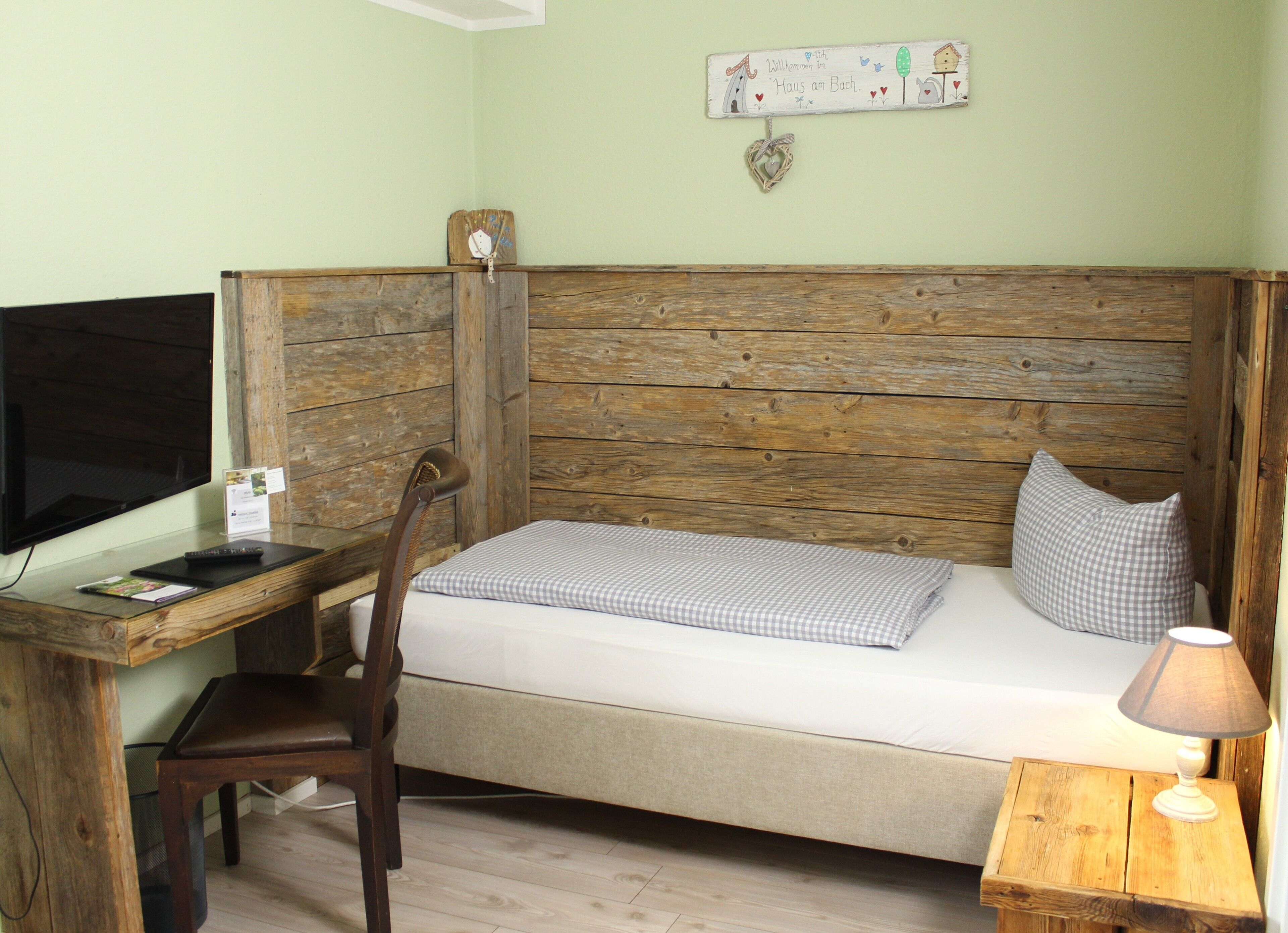 Une chambre avec un lit doté d’une tête de lit en bois, un bureau avec une chaise, une télévision et une petite table de chevet avec une lampe.