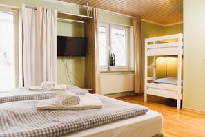 A hotel room with two beds, a TV, a window with curtains, and a bunk bed. - ARRIVEL Pension Haus am Bach (Allershausen)