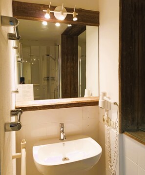 A bathroom with a white sink, a mirror, and a shower area. - ARRIVEL Pension Haus am Bach (Allershausen)
