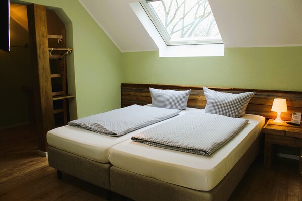 A bedroom with a skylight, two beds, wooden headboard, and a bedside lamp.
