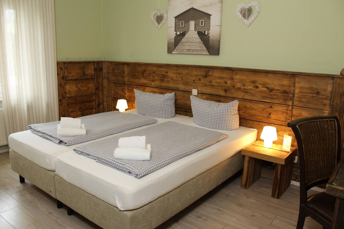 Ein Doppelbett mit karierter Bettwäsche, zwei Nachttischlampen, ein Holz-Kopfstück und herzförmige Wanddekorationen.