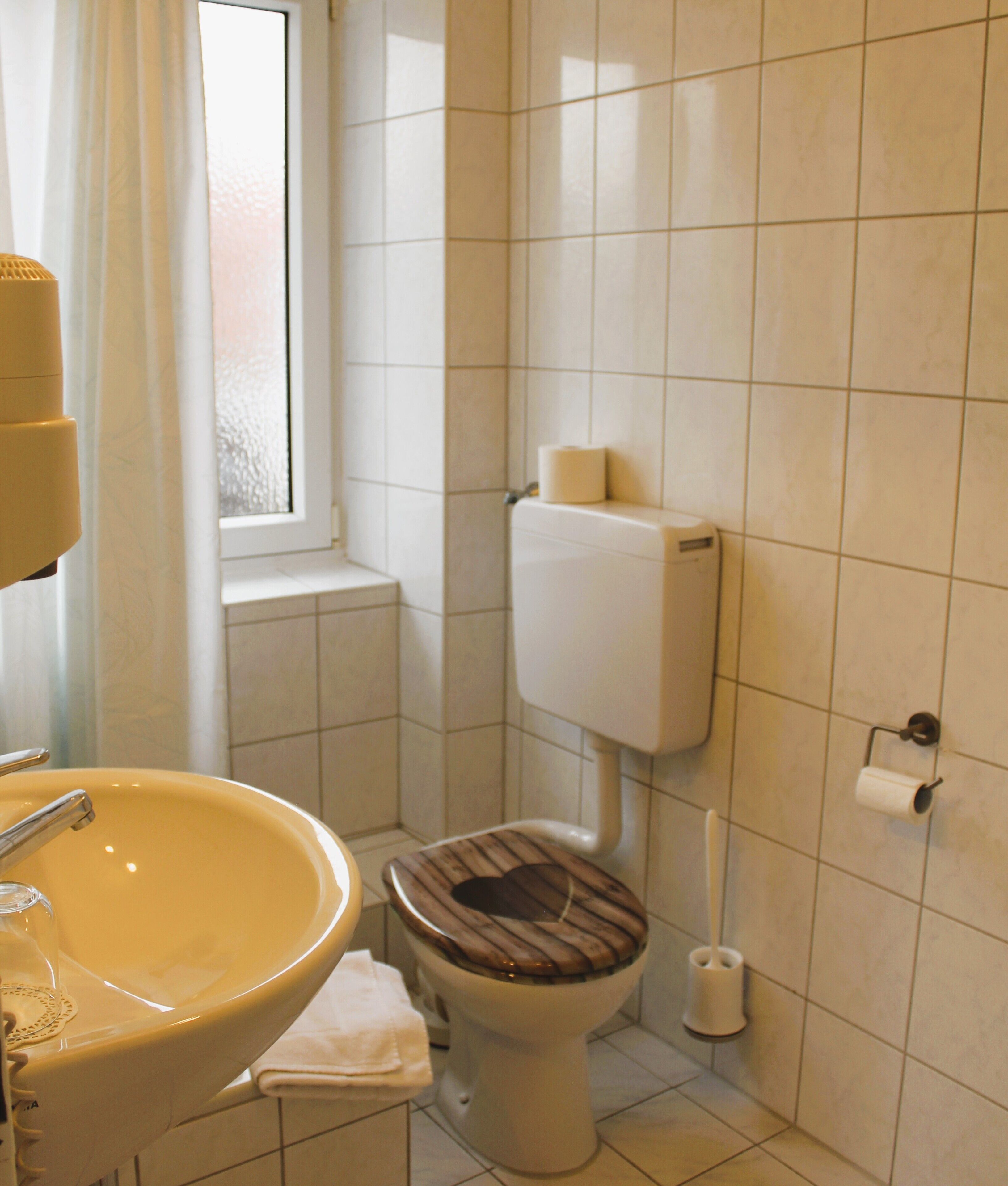 Un baño con un lavabo amarillo, un inodoro con asiento de madera y una ventana con cortina.