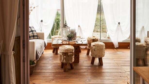 A cozy room with a wooden floor, a sofa, and a table with stools. - ARRIVEL Pension Haus am Bach (Allershausen)