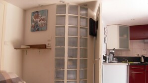 A bedroom with a bed, a bedside table, a wall-mounted TV, a kitchen area with cabinets, and a decorative wall panel. - Cielito Lindo (Montpellier)