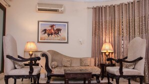 A living room with a sofa, two armchairs, a coffee table, and two lamps. There is a painting of a horse on the wall. - Islamabad inns (Islamabad)