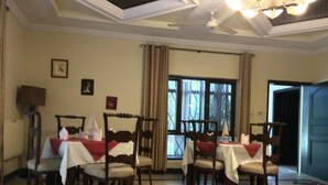 A hotel room with four wooden chairs, a table, a lamp, and a window with curtains. - Islamabad inns (Islamabad)