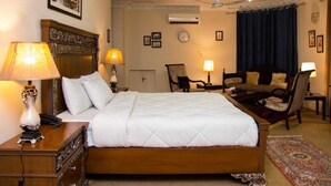 A hotel room with a large bed, two bedside tables with lamps, a chair, a small table, and a ceiling fan. - Islamabad inns (Islamabad)