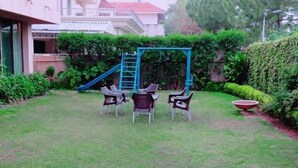 A grassy outdoor area with a swing set, a slide, and several chairs. - Islamabad inns (Islamabad)
