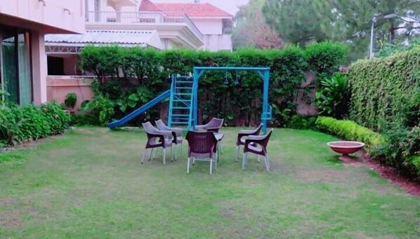 A grassy outdoor area with a swing set, a slide, and several chairs.
