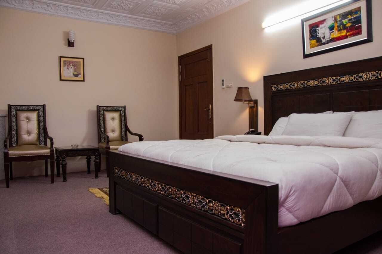 Un dormitorio con una cama grande, dos sillas, una mesita de noche, una lámpara y una puerta.
