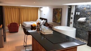 Una camera d'albergo moderna con un letto grande, un'area salotto con tavolo e sedie, una vasca da bagno e un muro in pietra.