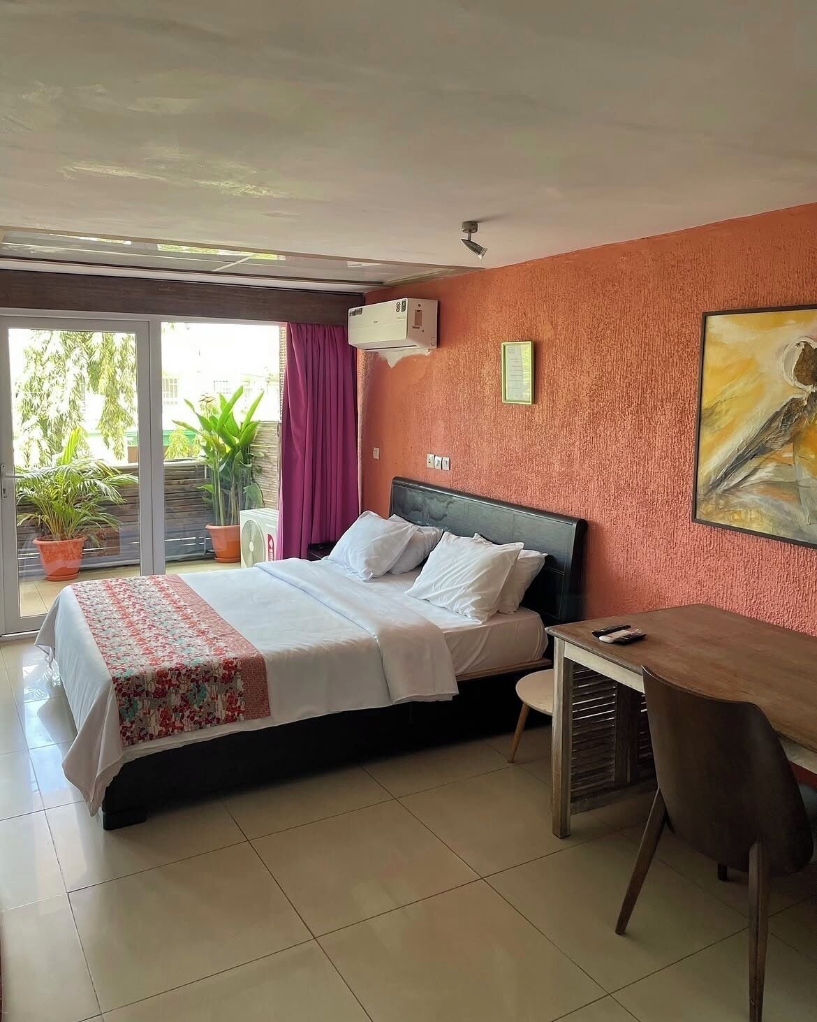 A bedroom with a bed, a desk, a chair, an air conditioning unit, and a window with curtains.
