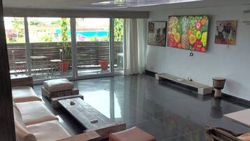 A spacious living area with a large flat-screen TV, comfortable seating, and a balcony with outdoor furniture.