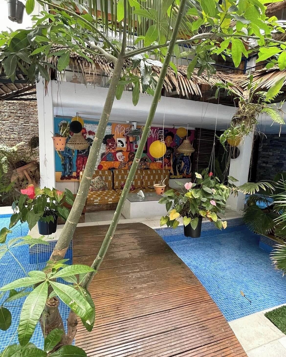 Un área de piscina con terraza de madera, rodeada de plantas en macetas y un mural.