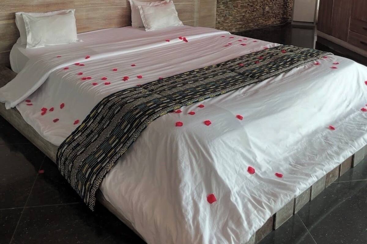 A hotel room with a stone wall, a bed with white bedding and rose petals, a wooden headboard, and a wardrobe.