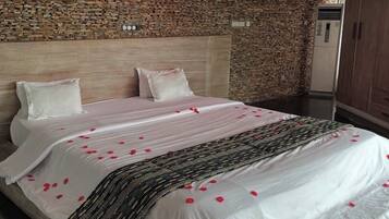 A hotel room with a stone wall, a bed with white bedding and rose petals, a wooden headboard, and a wardrobe.