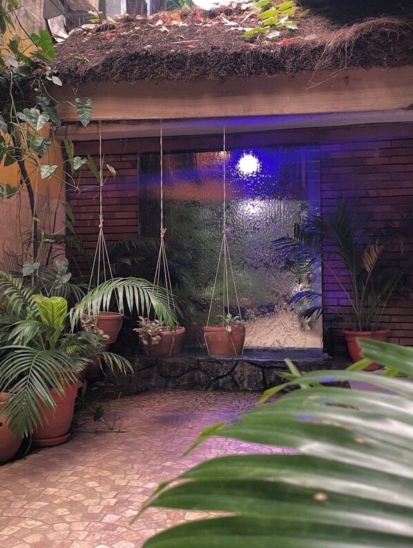 Un jardín con fuente de agua, plantas en macetas y un muro de ladrillo.