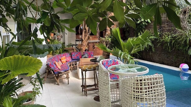 Patio esterno con mobili in vimini, piscina e rigogliosa vegetazione tropicale.