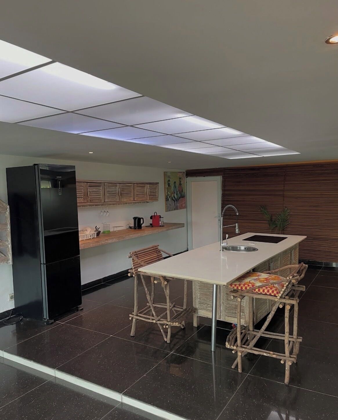 Une cuisine moderne avec un réfrigérateur noir, un îlot central blanc doté de tabourets de bar et un mur en bois.